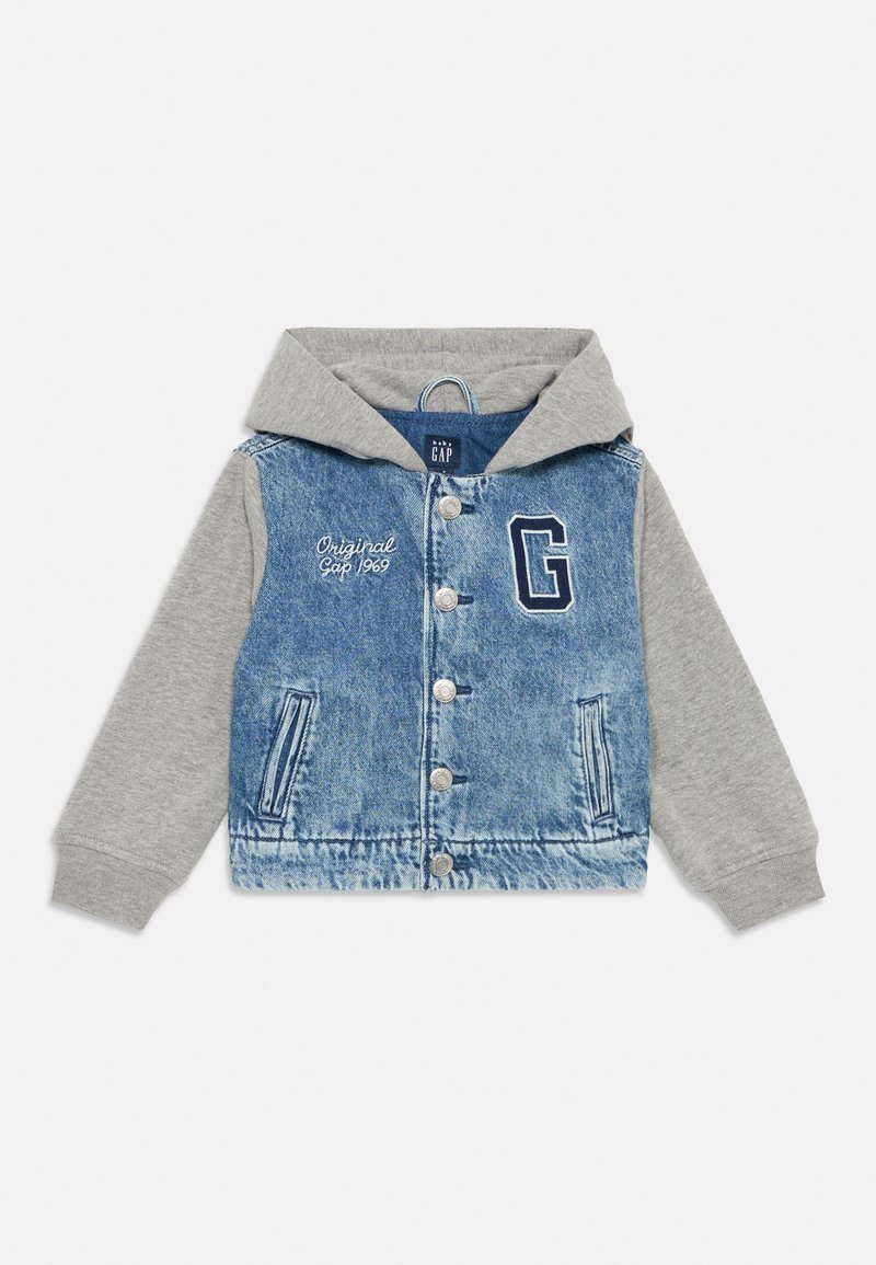 Džinsinis švarkas su pilku kapučinu. Yra mygtukai, dvi priekinės kišenės ir „G“ logotipas, su balta siuvinėtu užrašu „Original Gap 1969“.