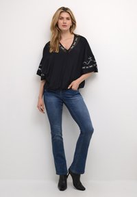 Blusa nera con dettagli ricamati argento lungo il collo e le maniche, abbinata a jeans svasati blu e stivaletti neri.