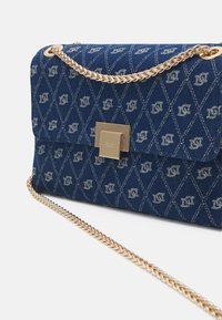 Niebieska torebka kopertówka w wzory z złotym łańcuszkiem i kwadratowym złotym zapięciem, ozdobiona geometrycznymi kształtami diamentów i małymi logo.