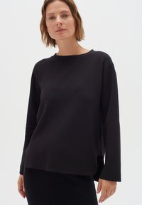 Maglia nera a maniche lunghe con collo a giro, texture morbida e spacchi laterali per maggiore comodità. Design minimalista con una vestibilità rilassata.