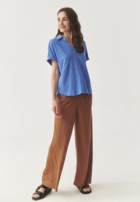 Polo shirt azzurro a maniche corte abbinato a pantaloni larghi marroni e sandali neri. La maglietta ha una vestibilità comoda e un colletto.