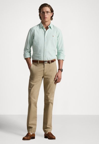 Light green striped button-down shirt, khaki pants, brown leather belt, and brown loafers. Glasses add detail to the polished look.