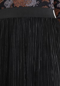 Svart plisserad kjol gjord av texturerad tyg. Bred, elastisk midja med vertikala plisseringar som skapar ett flödande utseende.