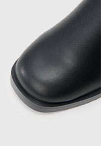 Μαύρο μποτάκι αστραγάλου με στρογγυλεμένη μύτη, κατασκευασμένο από λείο δέρμα, με υφή επιφάνειας και αντιθετική ελαστική σόλα.