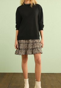 Felpa nera con maniche lunghe abbinata a una gonna a strati con stampa leopardata in beige e nero. Completata con stivali alla caviglia color crema.