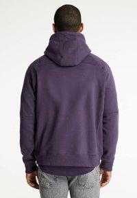 Sudadera morada con capucha ajustable, puños acanalados y corte relajado. Tejido suave, detalles de costura mínimos y textura lisa.
