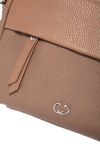 Primo piano di una borsa a tracolla marrone con superficie testurizzata, con una patta in pelle, due zip in pelle e un piccolo logo doppio-C in argento sulla superficie di tessuto.