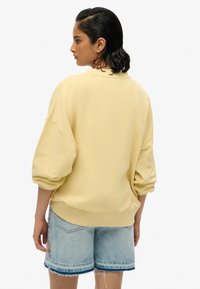 Felpa gialla con maniche oversize a sbuffo, bordo a coste e taglio rilassato. Abbinata a pantaloni shorts in denim blu chiaro con orlo sfilacciato.