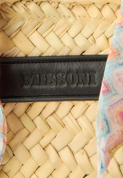 Πλεγμένη επιφάνεια από ψάθα με μαύρη δερμάτινη ετικέτα με ανάγλυφη την επιγραφή «MISSONI», μερικώς πλαισιωμένη από πολύχρωμο, μαλακό ύφασμα με ζιγκ-ζαγκ σχέδιο.
