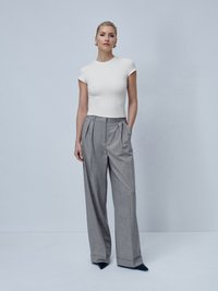 Top blanco ajustado de manga corta combinado con pantalones grises de cintura alta y con pliegues. Los pantalones tienen un corte amplio y dobladillos; zapatos negros de punta elegantes.