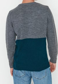 Trui met een grijs bovenstuk en een tealen onderstuk, gemaakt van een zachte gebreide stof met een geribbelde zoom en lange mouwen.