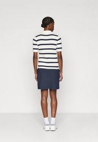 Csíkos kötött felső rövid ujjakkal, amely fehér és sötétkék vízszintes csíkokkal rendelkezik, egy egyszínű sötétkék szoknyával párosítva. Fehér sportcipővel viselve.