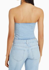 Blå denimkorsett-top med en axelbandslös design, åtsittande form och rå kant. Matchas med högmidjade blå jeans med standardfickor.