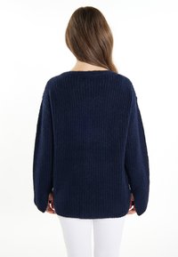 Sötétkék, oversized kötött pulóver, texturált bordás mintával, széles ujjak és kerek nyakkivágás, hátulról nézve.