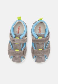 Graue Wildledersandalen mit blauer Einlage, Klettverschlüssen und gelben Akzenten. Offenes Design mit einer weißen Sohle für Atmungsaktivität und Komfort.