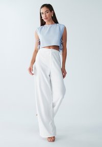 Lyseblå cropped top med korte ærmer og bånddetaljer, sammen med hvide bukser med bred benvidde i tekstureret stof. Brune open-toe sko.