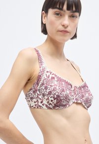 Σουτιέν σε κρεμ χρώμα με μπορντό ανθικό μοτίβο, διαθέτει διακοσμητικό τελείωμα, ενίσχυση με μπανέλες και ρυθμιζόμενους ιμάντες. Λείος υφασμάτινος και δομημένος σχεδιασμός.
