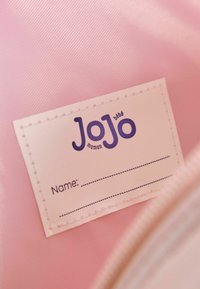 Wnętrze różowej torby nylonowej z białą metką z napisem "JoJo maman bb" w pogrubionym fioletowym tekście. Metka zawiera miejsce na imię.