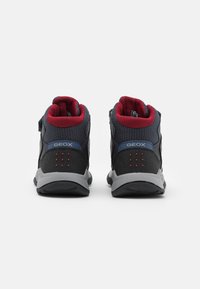 Czarne i szare buty mid-top z czerwonymi akcentami, z siateczkowego materiału i teksturowanym obcasem. Posiadają otwory wentylacyjne i mocną gumową podeszwę.