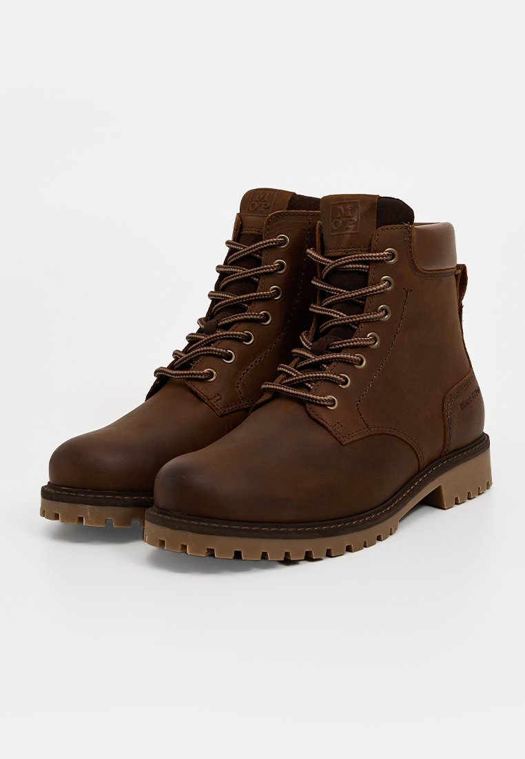 Ein Paar braune Leder-Schnürstiefeletten mit gepolstertem Kragen und robusten Gummisohlen auf einem weißen Hintergrund.