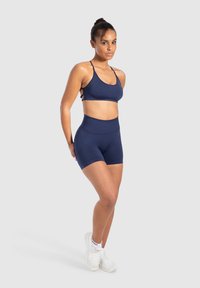 Sujetador deportivo azul marino y pantalones cortos de cintura alta hechos de material elástico; cuenta con tirantes finos y una textura suave, combinados con zapatillas blancas.