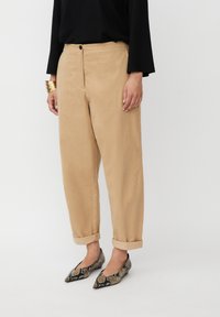 Beige linnen broek met een relaxte pasvorm, voorzien van een knoopsluiting, omgeslagen uiteinden en een soepele textuur. Gepaard met puntige, slangenprint instappers.