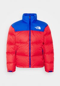 Veste rembourrée rouge et bleue avec un col haut, fermeture éclair sur le devant et le logo The North Face sur la poitrine. Comprend des poignets élastiques et un contraste de texture.