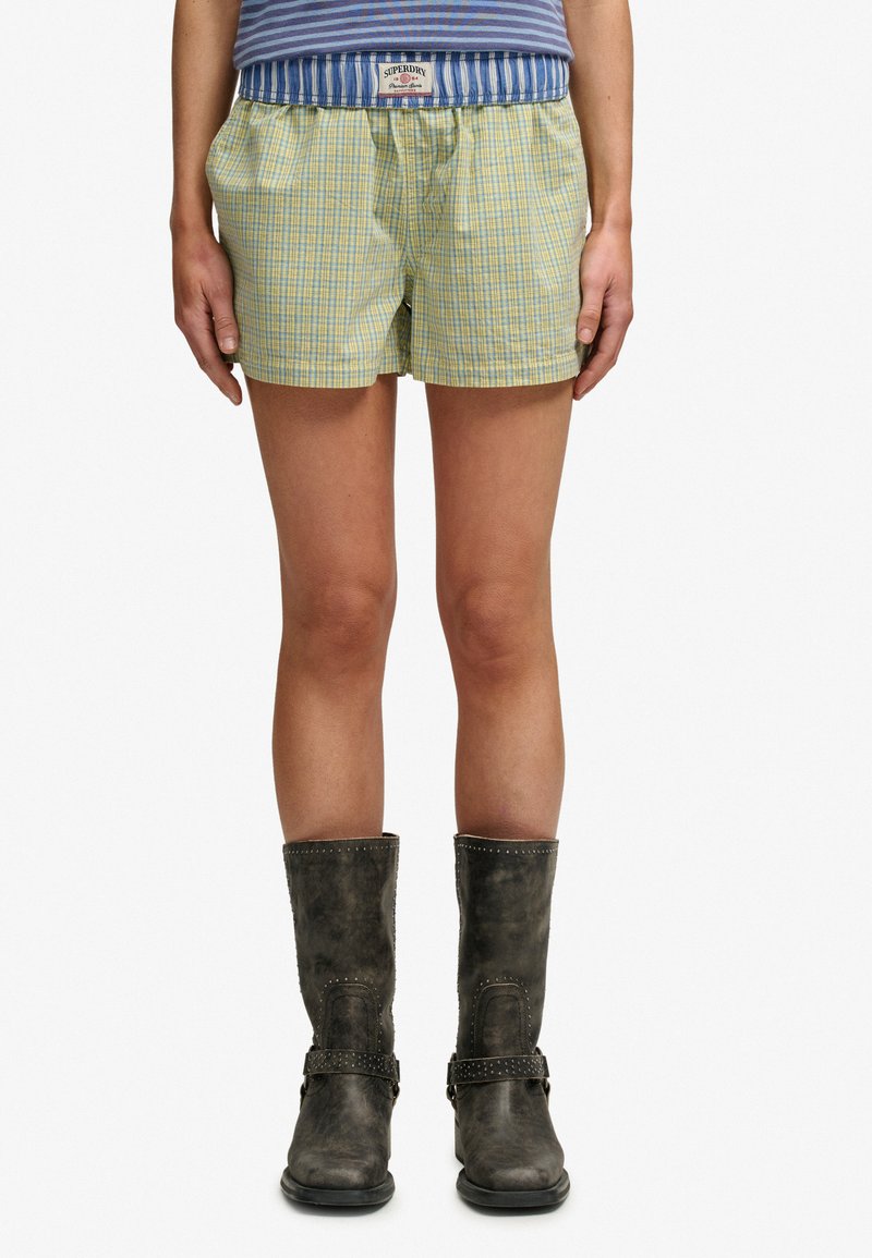 Person wearing yellow and blue plaid shorts, a blue and white striped top, and dark mid-calf boots with buckle details.