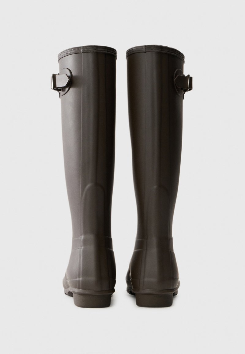 Ein Paar hohe, dunkelbraune Gummiregenstiefel von hinten betrachtet, jeweils mit einem verstellbaren Seitenriemen nahe der Oberseite.