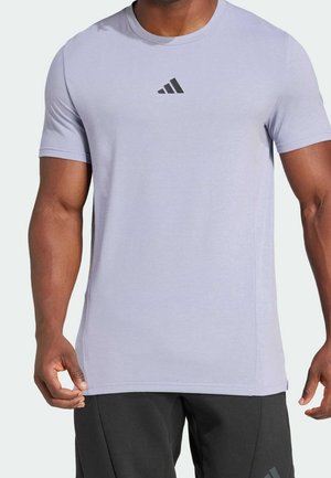Homme portant un t-shirt de sport à manches courtes violet clair avec un petit logo Adidas noir sur la poitrine et un pantalon noir.