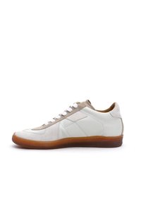 Weiße Ledersneaker mit Wildlederakzenten, beigem Rand, flachen Schnürsenkeln und einer strukturierten braunen Gummisohle. Die Seitenansicht zeigt die Designdetails.