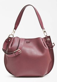 Fioletowa skórzana torba na ramię z regulowanym paskiem, złotymi akcesoriami oraz dekoracyjnym charmsiem z inicjałami marki.