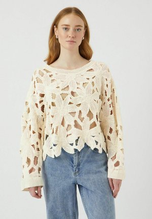 Gehaakt vest in crèmekleur met een bloemmotief, open breiselontwerp, brede mouwen en een ribgebreide halslijn, gecombineerd met hoogzitter denim jeans.