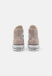 High-top canvas sneakers in light beige, featuring a white rubber sole, black stripes, and a round logo patch on heel.