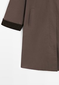 Cappotto esterno marrone con una texture liscia, caratterizzato da una vestibilità dritta, tasche laterali e polsini in corduroy scuro.