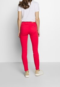 Rosa skinny jeans med slim fit och bakfickor, tillsammans med en vit T-shirt och beiga sneakers, sedd bakifrån.