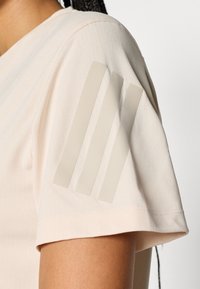 Beige sportshirt met korte mouwen en een gestructureerde stof, met drie doorzichtige strepen op de linkerschouder.