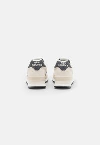 Beżowe zamszowe sneakersy z szarymi akcentami, z amortyzowanym obcasem i czarną gumową podeszwą, z logo "new balance" na obcasie.