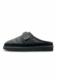 Zwarte slipper met een gevoerde bovenkant, voorzien van een klittenbandsluiting, een gestructureerde afwerking en een dikke rubberen zool met een geprofileerd patroon.