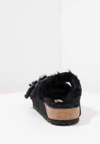Chinelo preto com uma textura macia, sola de cortiça, design de costas abertas e forro semelhante a pelo. Apresenta um pequeno salto e palmilha suave.