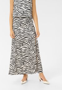 Rockiger Rock aus zebra-farbenem Stoff mit einem seitlichen Schlitz, kombiniert mit einem passenden Oberteil. Schwarz-weiße Farbkombination, ergänzt durch elegante High Heels mit metallic Akzenten.