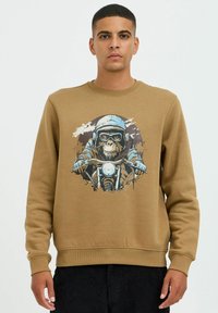 Brun sweatshirt med grafik af en abe, der kører på motorcykel, med blå og sorte accenter. Fremstillet af blødt, tekstureret stof.