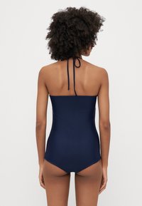 Jūras spēku stilā šiks vientilpnis peldkostīms ar kakla saiti, vienkrāsainu tekstūru un elegantu dizainu, kas izceļ ķermeni.