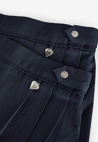 Pantaloni blu navy con pieghe laterali, zip a forma di cuore argentate e bottoni personalizzati. Il tessuto ha una texture liscia.