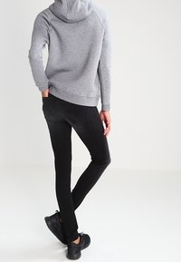 Felpa grigia con cappuccio, jeans neri slim-fit e sneakers nere. La felpa ha una tasca a marsupio; i jeans presentano tasche posteriori e una texture liscia.