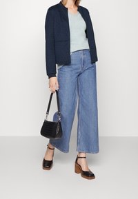 Granatowa pikowana kurtka, jasnoniebieski top z dekoltem w serek, szerokie dżinsy o kroju dzwonów, czarna torebka z tłoczonym wzorem krokodyla oraz czarne chodaki na drewnianych obcasach.