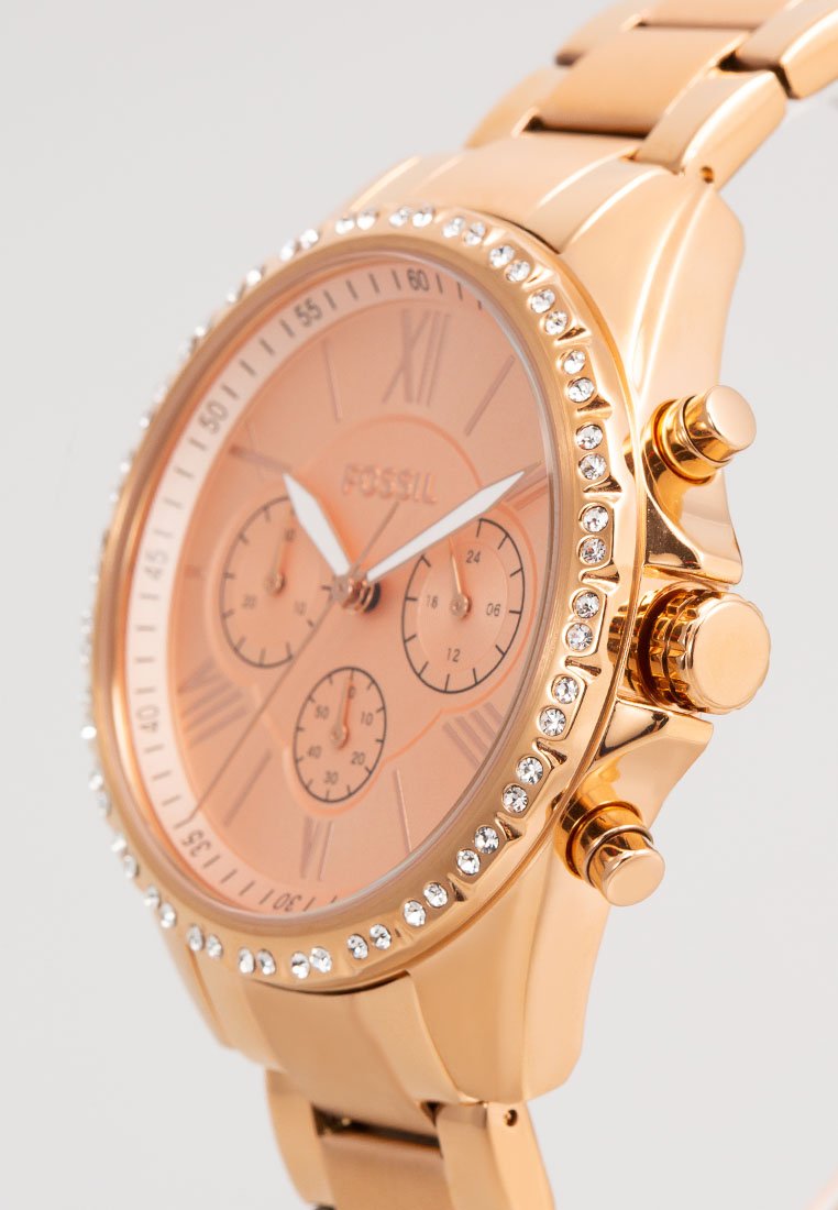 Roze gouden horloge met een ronde wijzerplaat, Romeinse cijfers, drie subdialen en strasaccenten. Metalen band met een gepolijst afwerking.