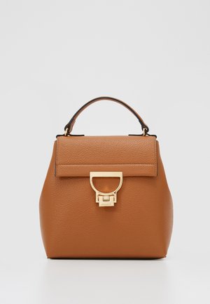 Średniej wielkości brązowa skórzana torebka z górnym uchwytem i złotą prostokątną klamrą z przodu na jasnym, prostym tle.
