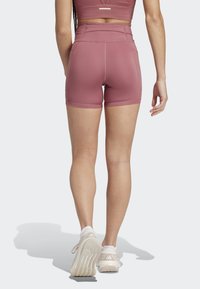 Højtaljede, rosenfarvede træningsshorts med en glat overflade og veldefinerede syninger. Bæres med lyse sportsko.