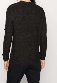 Maglione nero, strutturato, con scollo rotondo e maniche lunghe. Presenta un motivo a maglia e polsini e orlo a coste.